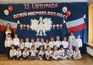 Dzieci wspólnie z Panią pozują na tle orła białego, polskich flag oraz napisu 11 listopada Dzień Niepodległości.