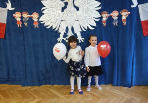 Dwie dziewczynki pozują na tle orła białego, polskich flag oraz napisu 11 listopada Dzień Niepodległości.