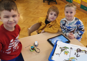 Trzech chłopców prezentuje zbudowanego robota z klocków lego na warsztatach z robotyki.