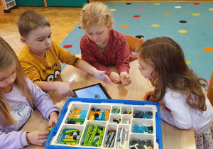 Dzieci siedzą przy stoliku I budują robota z klocków lego na podstawie wyświetlanych zdjęć na tablecie.