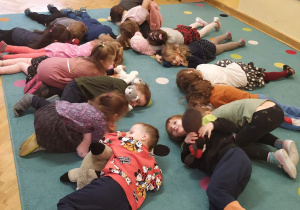 Dzieci leżą na dywanie ze swoimi misiami po wykonanej gimnastyce porannej.