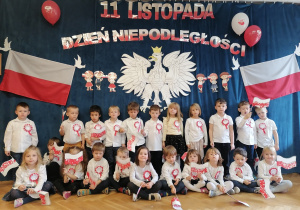 Dzieci pozują na tle orła białego, polskich flag oraz napisu 11 listopada Święto Niepodległości.
