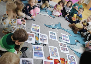 Dzieci siedzą na dywanie w kole i oglądają obrazki misiów występujących w bajkach dla dzieci.
