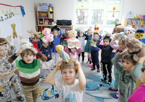 Dzieci tańczą do szybkiej piosenki z misiami na głowach.