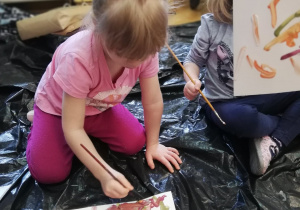 Dziewczynka maluje farbami dowolny malunek, a druga pokazuje skończoną pracę.