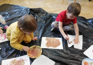 Chłopcy siedzą na folii i malują farbami dowolny malunek.