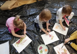 Dziewczynki siedzą na folii i malują farbami dowolny malunek.