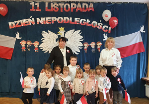 Dzieci wspólnie z Paniami pozują na tle orła białego, polskich flag oraz napisu 11 listopada Dzień Niepodległości.