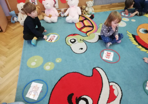 Dzieci siedzą na dywanie prezentując ułożone misiowe puzzle.