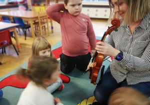 Dzieci siedzą na dywanie i oglądają skrzypce.
