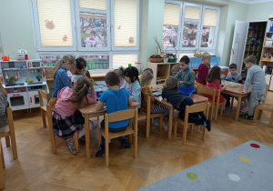 Dzieci siedzą przy stolikach i układają klocki LEGO na zajęciach z robotyki.