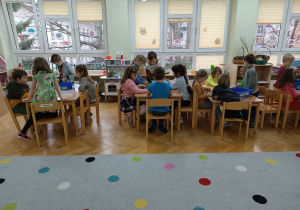 Dzieci siedzą przy stolikach i próbują stworzyć konstrukcje z klocków LEGO na zajęciach z robotyki.