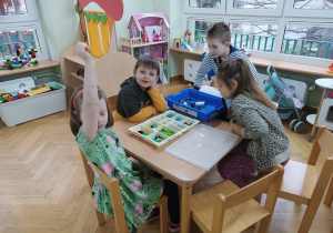 Dwie dziewczynki i dwóch chłopców siedzi przy stoliku i próbuje zbudować konstrukcje z klocków LEGO na zajęciach z robotyki.