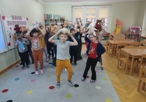Dzieci tańczą do szybkiej piosenki ze swoimi misiami na głowach.