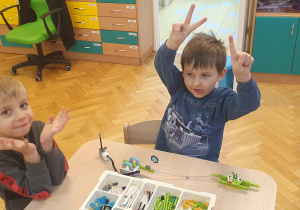 Dwóch chłopców prezentuje robota wykonanego z klocków lego na warsztatach z robotyki.