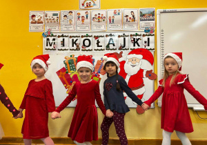 Zabawa muzyczna do piosenki "6 grudnia". Dzieci poruszają się po sali w rytm muzyki trzymając się za ręce ubrane w czapki Mikołaja.