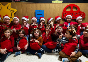 Dzieci siedzą w dwóch rzędach prezentują prezenty od Świętego Mikołaja.