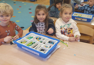Dzieci siedzą przy stole i budują roboty z klocków lego.