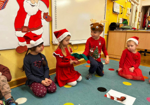 Dzieci siedzą na dywanie i bawią się z czapką elfa.