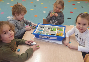 Dzieci siedzą przy stole I budują z klocków na warsztatach z robotyki.