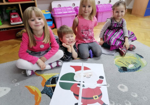 Trzy dziewczynki i chłopiec prezentują ułożone przez siebie puzzle ze Świętym Mikołajem.