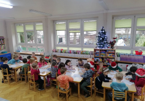 Dzieci siedzą przy stolikach i wykonują kartę pracy o tematyce świątecznej.