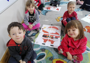 Dwóch chłopców i dwie dziewczynki prezentują ułożone przez siebie puzzle ze Świętym Mikołajem.