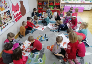 Dzieci siedzą na dywanie i w małych czteroosobowych grupkach układają puzzle z postacią Świętego Mikołaja.
