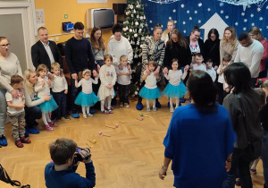 Dzieci wspólnie z Rodzicami stoją w kole i śpiewają razem kolędy.