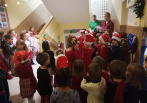 Dzieci stoją na korytarzu przedszkolnym i słuchają, jak Pani dyrektor czyta im list od Świętego Mikołaja.