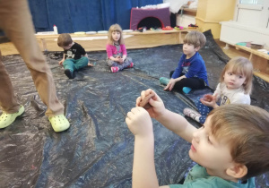 Dzieci siedzą na folii i lepią różne figurki z gliny.