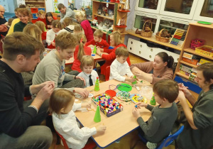 Dzieci wspólnie z Rodzicami ozdabiają styropianową choinkę kolorowymi pomponami, cekinami, naklejkami i kokardkami podczas warsztatów świątecznych.