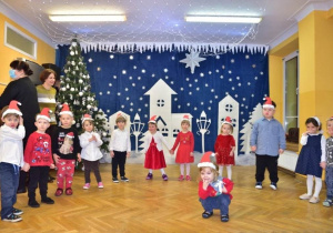 Dzieci podczas występu świątecznego stoją ustawione w półkolu i prezentują swój świąteczny repertuar piosenek.