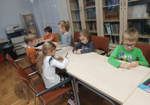 Dzieci przy stolikach wykonują pracę plastyczną - zakładkę do książki.