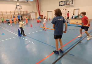 Dzieci wykonują ćwiczenia gimnastyczne na urządzeniach sportowych podczas zajęć sportowych na sali gimnastycznej w Szkole Podstawowej nr 210.