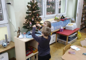 Dwóch chłopców dekoruje choinkę zawieszając bombki.