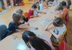Dzieci przy stolikach wykonują pracę plastyczną w kształcie głowy renifera.