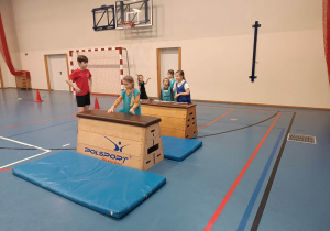 Dzieci wykonują ćwiczenia gimnastyczne na urządzeniach sportowych podczas zajęć sportowych na sali gimnastycznej w Szkole Podstawowej nr 210.