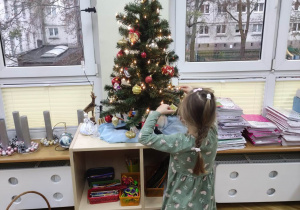 Dziewczynka dekoruje choinkę zawieszając bombki.