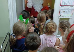 Dzieci stoją przy drzwiach i witają się ze Świętym Mikołajem.