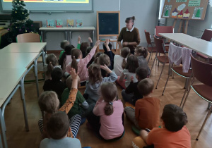 Dzieci siedzą na podłodze i rozmawiają z Panią na temat książek dla dzieci.