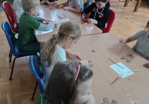 Dzieci przy stolikach wykonują pracę plastyczną w kształcie głowy renifera.