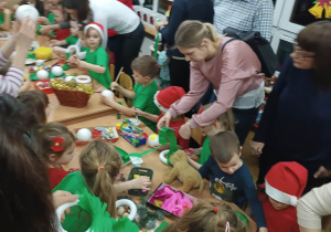 Dzieci z pomocą rodziców wykonują dekorują bombki styropianowe oraz świąteczne stroiki z bombek, piórek, cekinów, kolorowego papieru i kolorowych pomponów podczas warsztatów świątecznych.