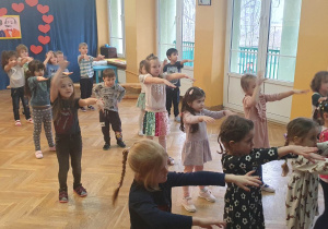 Dzieci tańczą na zajęciach zumby z rękami wyciągniętymi do przodu.