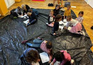 Dzieci siedzą na podłodze, kolorują plakaty- afisze do opery.
