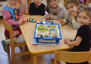 Dziewczynki siedzą przy stoliku i prezentują żuka zrobionego z klocków lego.