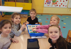 Dziewczynki siedzą przy stoliku i układają z klocków lego budowlę.