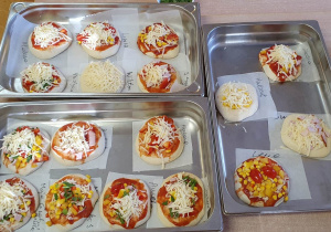Zrobione przez dzieci pizze są w blaszce przygotowane do upieczenia.