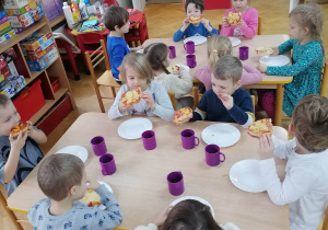 Dzieci siedzą przy stolikach i zajadają się własnoręcznie wykonanymi pizzami z okazji Światowego Dnia Pizzy.