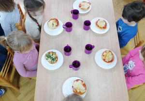 Dzieci siedzą przy stolikach i przyglądają się wykonanym przez siebie pizzą z okazji Światowego Dnia Pizzy.